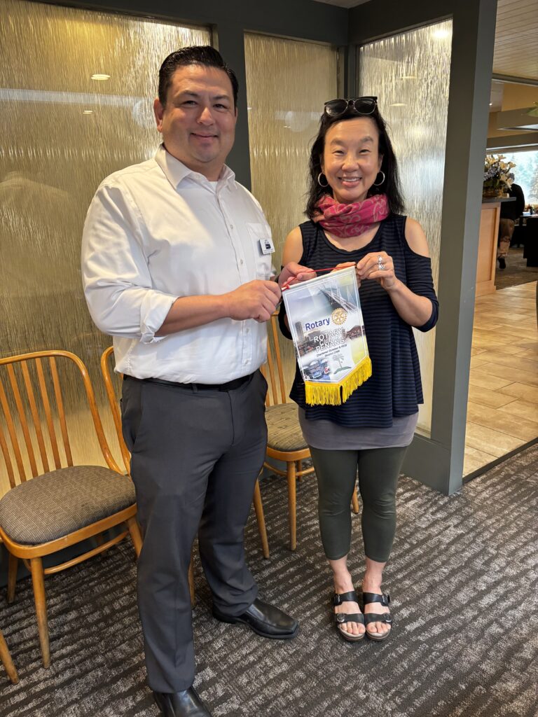 President-Elect Tinling Choong presents President Jeff Nielsen with a club banner from the Rotary Club of Penang, Malaysia after her recent trip there.